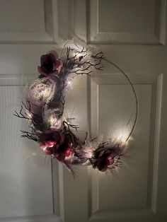 a wreath with flowers and branches hanging on the front door, lit up by fairy lights