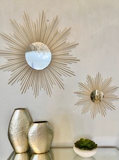 two sunburst mirrors on the wall above a table with vases and plants