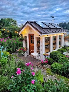 a small white shed sitting in the middle of a lush green yard with pink flowers