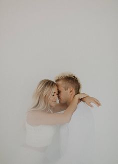 a man and woman embracing each other in front of a white wall