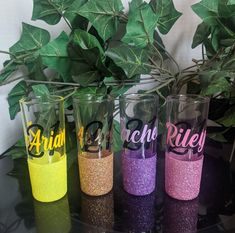 three different colored glasses sitting on top of a table next to a potted plant