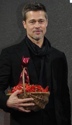 a man in a black suit holding a basket with red flowers on it and smiling at the camera