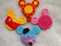 three crocheted mickey mouses are shown on the floor, one is red, one is yellow and one is blue