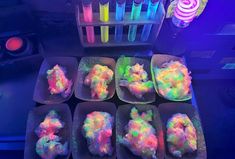 several trays filled with different colored powder in front of some neon sticks and other items