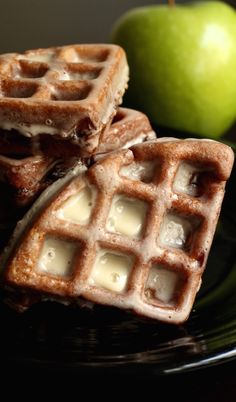 two waffles on a black plate with an apple in the backgroud