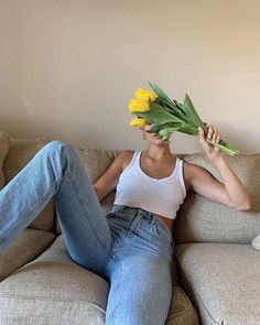 a woman sitting on top of a couch holding yellow flowers in front of her face