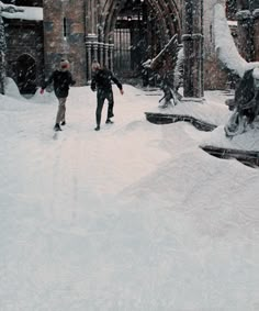 two people walking through the snow in front of a building