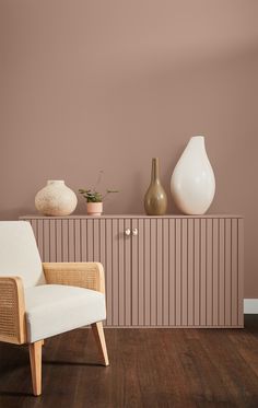 a white chair sitting in front of a wall with vases on top of it