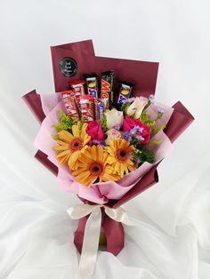 a bouquet of flowers and chocolates wrapped in red paper on a white cloth background