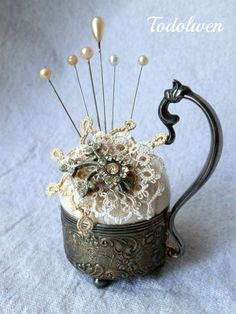 an old fashioned teapot is adorned with pins and lace, as well as pearls