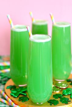 three glasses filled with green liquid sitting on top of a wooden tray next to straws