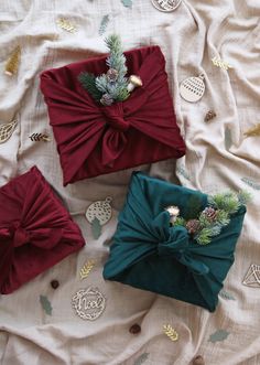 three presents wrapped in red and green bows on a white sheet with pineconis