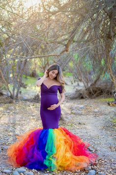 a pregnant woman in a purple gown poses for the camera while wearing a rainbow colored dress