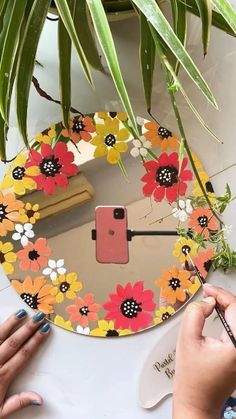 a person painting flowers on a mirror with paintbrushes next to a potted plant