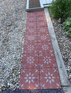 a red walkway with white flowers painted on it and some plants in the back ground