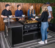 four people are gathered around an outdoor grill