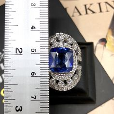 a blue and white diamond ring sitting on top of a measuring tape next to a ruler