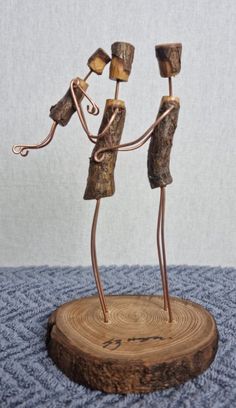 two wooden figurines are holding hands and standing on a piece of drift wood