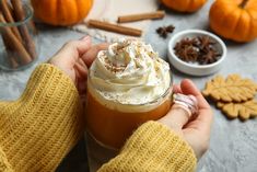 a person holding a drink with whipped cream and cinnamons around it on a table