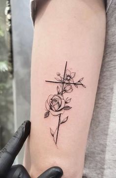 a woman's arm with a cross and roses tattoo on the left side of her arm