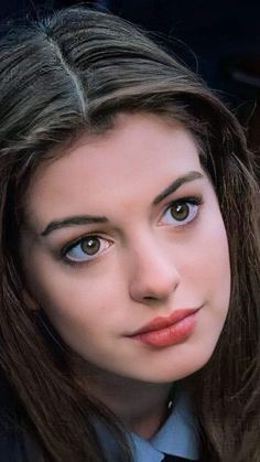 a woman with long hair wearing a blue shirt and black tie looking at the camera