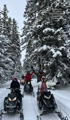 three people riding snowmobiles on a snowy road