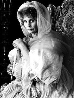 an old black and white photo of a woman sitting in a chair wearing a veil