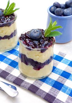 two small jars filled with blueberry cheesecake and topped with fresh mint sprigs