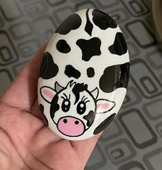 a hand holding a black and white cow painted rock