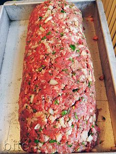 an uncooked meatloaf covered in sauce and herbs