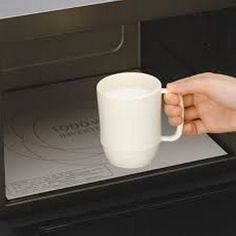 a person is holding a coffee mug in front of a microwave with the door open