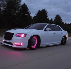 a white car driving down the road with pink lights on it's front end