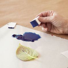 a person is holding a paint brush and painting leaves on paper with blue inks