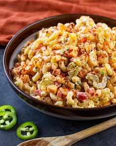 a bowl filled with macaroni salad next to green peppers and a wooden spoon