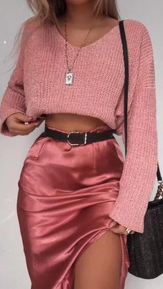 a woman wearing a pink sweater and skirt with high slits, holding a black purse