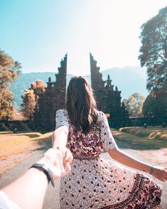 a woman holding the hand of a man who is walking down a road with trees in the background