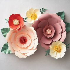 three paper flowers with green leaves on them