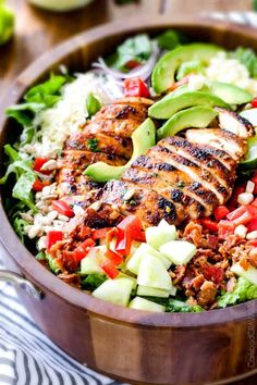 a salad with chicken, avocado, tomatoes and cucumber in a wooden bowl