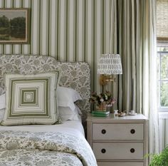 a bedroom with green and white striped wallpaper, bedding, dresser and window