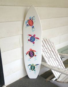 a white surfboard with sea turtles painted on it next to a chair and wall