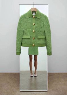 a woman's reflection in a mirror with a green jacket and skirt on it