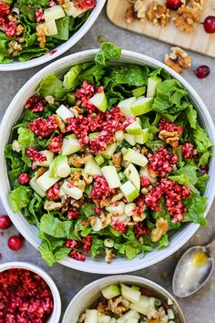 three white bowls filled with salad next to some cranberries and walnuts on a cutting board