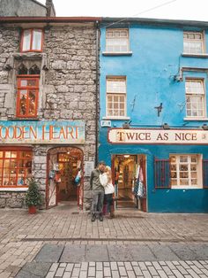 two people standing in front of a blue and grey building with shops on each side