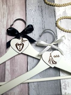 two wooden wedding hangers with black and white designs on them, one has a bride and groom's dress hanging from it