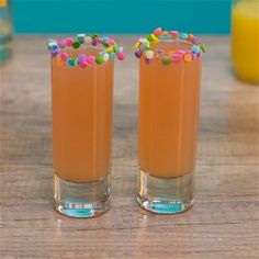 two glasses filled with orange juice and sprinkles on top of a wooden table