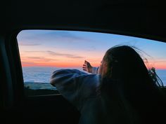 a woman sitting in the back seat of a car looking out at clouds and sunset