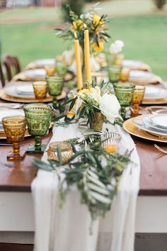 the table is set with green and gold plates, silverware, and greenery