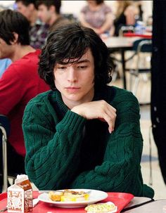 a young man sitting at a table in front of a plate with food on it