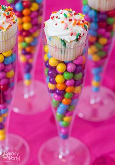 cupcakes with sprinkles and candy are in wine glasses on a pink table