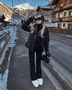 a woman standing on the side of a road wearing skis and holding her hat